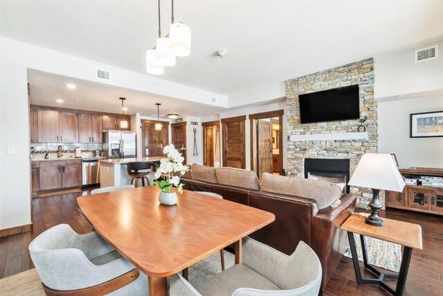 dining room with a stone fireplace, dark wood finished floors, and visible vents