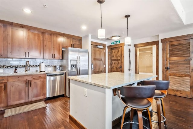 kitchen featuring a sink, stainless steel appliances, hanging light fixtures, and a kitchen island