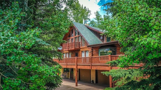 rear view of house with log exterior, driveway, an attached garage, and roof with shingles