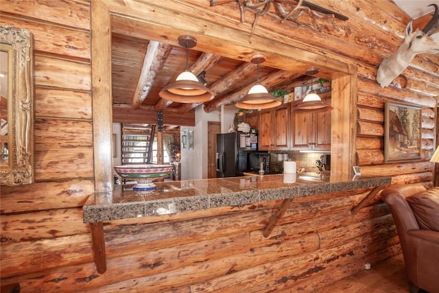 kitchen with beam ceiling, black fridge with ice dispenser, rustic walls, tile countertops, and wooden ceiling