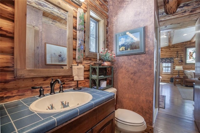 bathroom with vanity, toilet, wood finished floors, and rustic walls