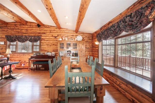 dining area featuring log walls, beam ceiling, hardwood / wood-style flooring, and a healthy amount of sunlight