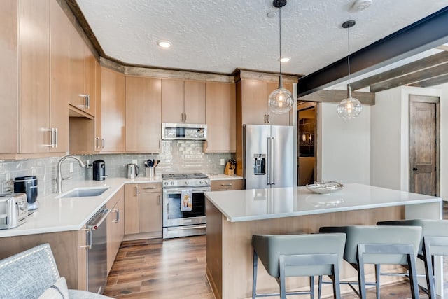 kitchen with light brown cabinetry, hanging light fixtures, appliances with stainless steel finishes, sink, and a kitchen island