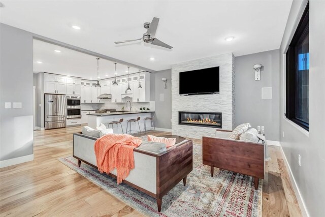 living room with ceiling fan, light hardwood / wood-style floors, a stone fireplace, and sink