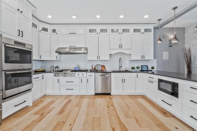 kitchen with kitchen peninsula, stainless steel appliances, a barn door, white cabinetry, and hanging light fixtures