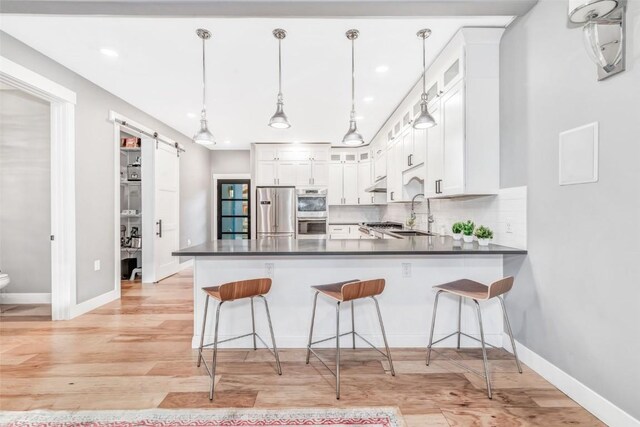 kitchen with kitchen peninsula, stainless steel appliances, a barn door, white cabinetry, and hanging light fixtures