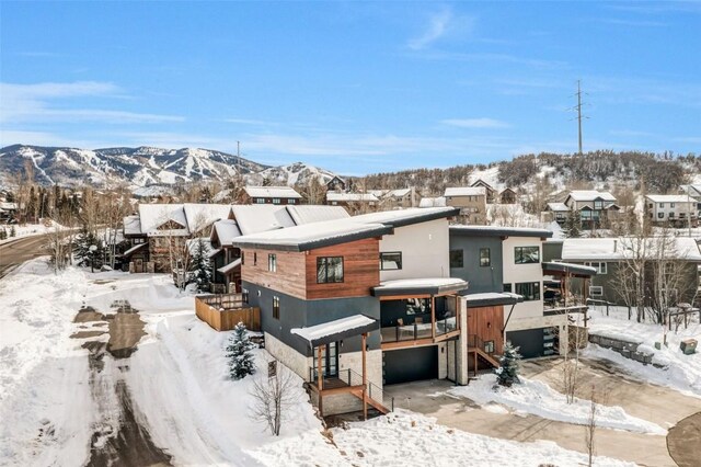 snow covered rear of property featuring a mountain view, an attached garage, and a residential view