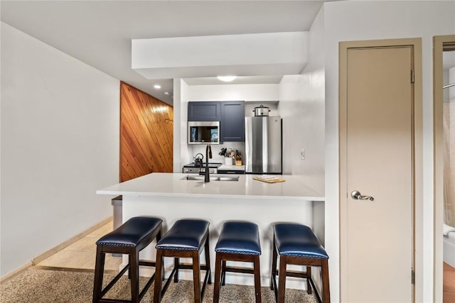 kitchen with a kitchen bar, sink, light tile patterned floors, appliances with stainless steel finishes, and kitchen peninsula