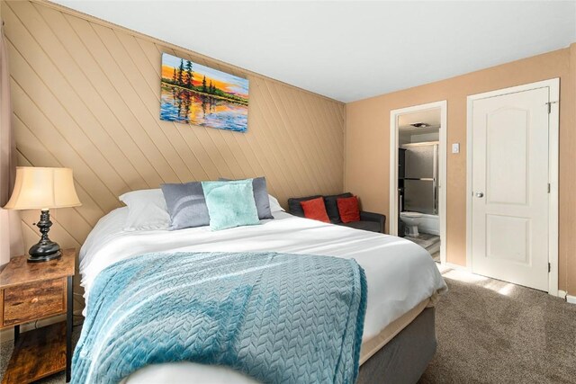 carpeted bedroom featuring ensuite bathroom and wood walls