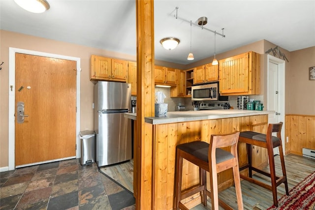 kitchen with hanging light fixtures, stainless steel appliances, a kitchen breakfast bar, kitchen peninsula, and track lighting