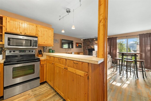 kitchen featuring rail lighting, light hardwood / wood-style flooring, a fireplace, appliances with stainless steel finishes, and kitchen peninsula