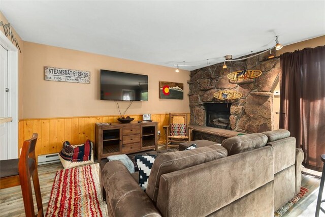 living room with a stone fireplace, a baseboard radiator, track lighting, and hardwood / wood-style flooring