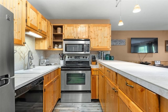 kitchen featuring tasteful backsplash, stainless steel appliances, sink, decorative light fixtures, and light hardwood / wood-style flooring