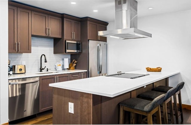 kitchen featuring appliances with stainless steel finishes, island range hood, tasteful backsplash, sink, and a kitchen breakfast bar