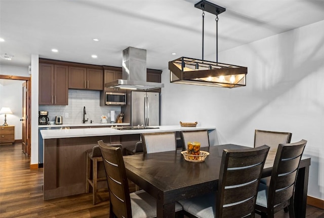 kitchen featuring appliances with stainless steel finishes, dark brown cabinets, tasteful backsplash, island range hood, and decorative light fixtures