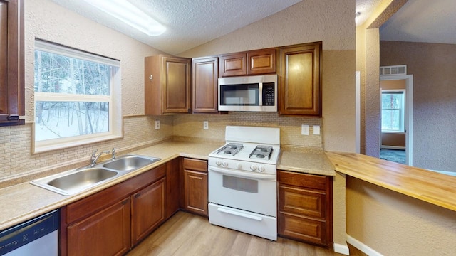 kitchen featuring sink, appliances with stainless steel finishes, tasteful backsplash, vaulted ceiling, and light wood-type flooring