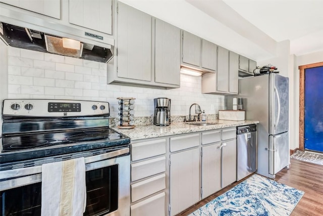 kitchen with sink, backsplash, stainless steel appliances, light stone countertops, and light hardwood / wood-style flooring