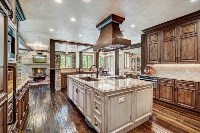 kitchen featuring light stone counters, a kitchen island with sink, dark wood-type flooring, sink, and a fireplace