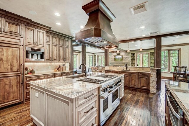 kitchen featuring premium range hood, a kitchen island with sink, range with two ovens, dark hardwood / wood-style floors, and light stone countertops