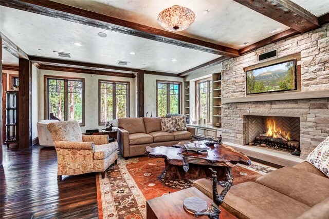 living room with built in shelves, dark wood-type flooring, a stone fireplace, and ornamental molding