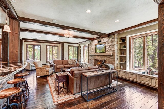 living room featuring beamed ceiling, built in features, dark wood-type flooring, and a stone fireplace