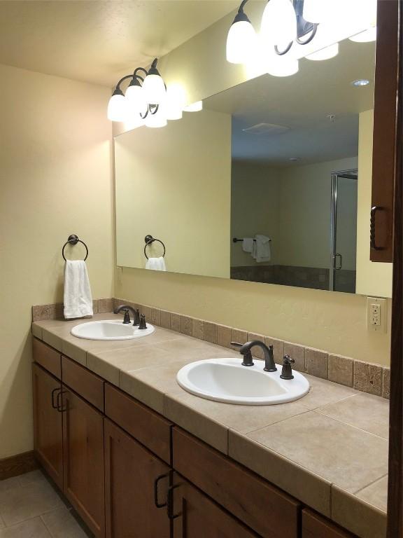 bathroom with double vanity, a shower stall, tile patterned floors, and a sink