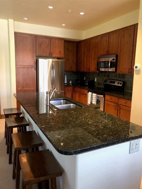 kitchen with backsplash, appliances with stainless steel finishes, dark stone counters, and a sink