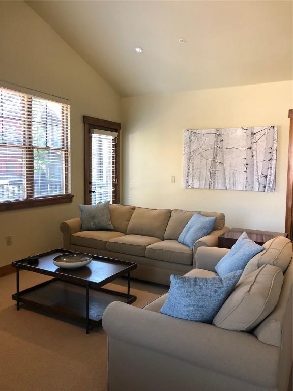 living room featuring carpet floors, baseboards, and vaulted ceiling