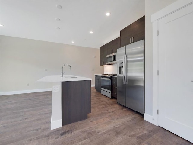 kitchen featuring sink, hardwood / wood-style flooring, stainless steel appliances, dark brown cabinets, and a center island with sink