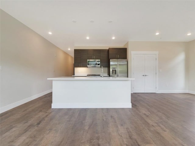 kitchen with dark brown cabinetry, appliances with stainless steel finishes, a kitchen island with sink, and hardwood / wood-style floors