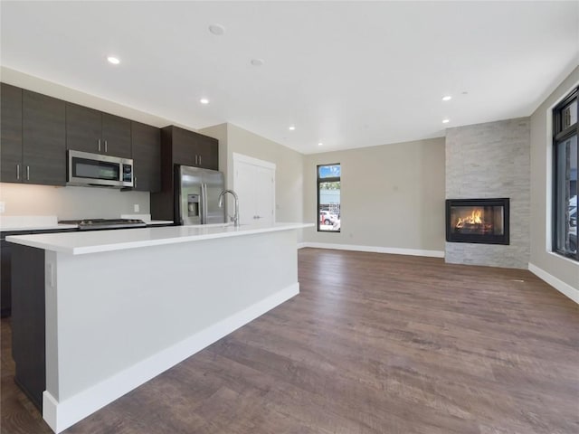 kitchen with stainless steel appliances, a fireplace, dark hardwood / wood-style flooring, and a kitchen island with sink