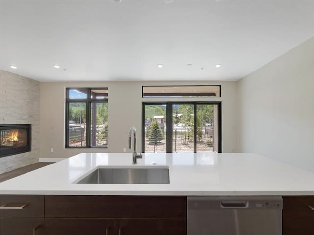 kitchen featuring dark brown cabinetry, sink, dishwasher, an island with sink, and a fireplace