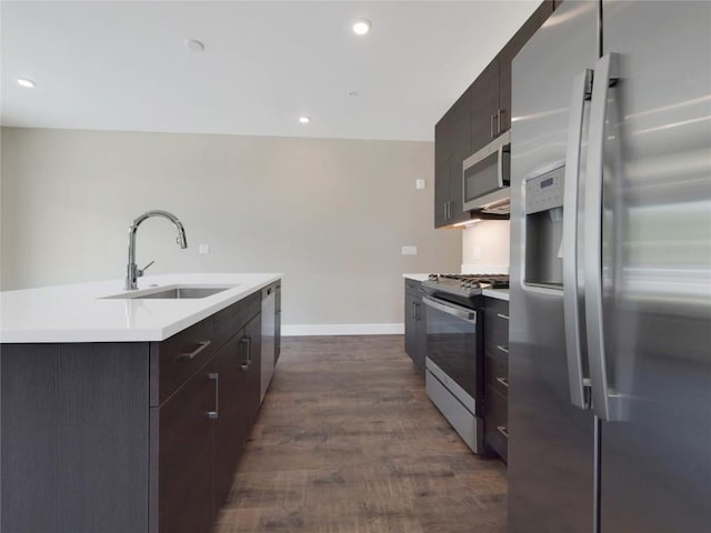 kitchen featuring appliances with stainless steel finishes, dark hardwood / wood-style floors, sink, dark brown cabinets, and a center island with sink