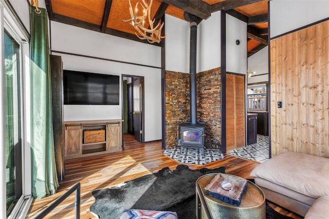 living area featuring beam ceiling, a chandelier, a wood stove, and wood finished floors