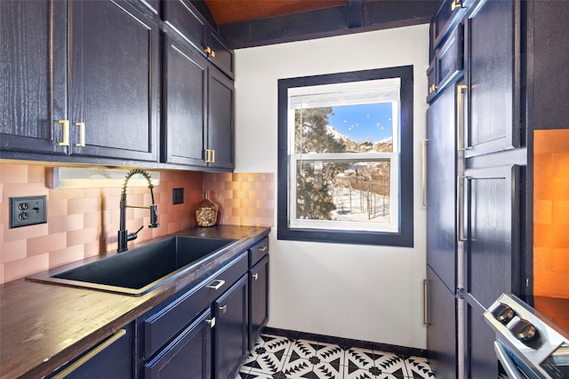 kitchen featuring stainless steel range, a sink, dark countertops, decorative backsplash, and baseboards