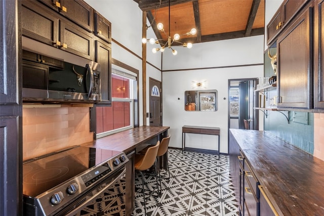 kitchen with beamed ceiling, a notable chandelier, stainless steel appliances, decorative backsplash, and dark brown cabinets