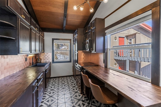 kitchen featuring stainless steel microwave, butcher block counters, decorative backsplash, electric stove, and a sink