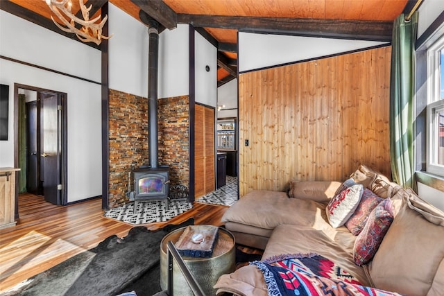 unfurnished living room with lofted ceiling with beams, a wood stove, wood finished floors, and wood walls