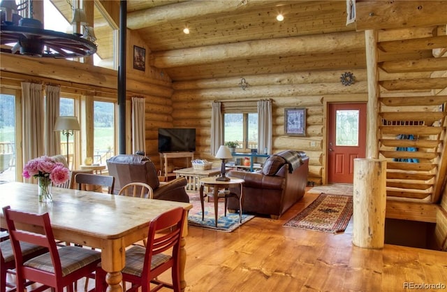 dining area with log walls, wood-type flooring, vaulted ceiling, and plenty of natural light