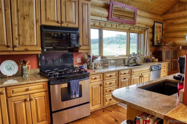 kitchen featuring lofted ceiling, sink, rustic walls, appliances with stainless steel finishes, and light hardwood / wood-style floors