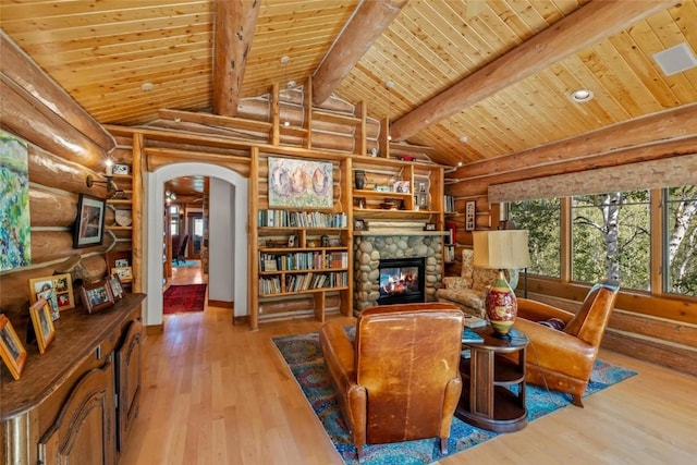 sitting room featuring a stone fireplace, vaulted ceiling with beams, wood ceiling, and light hardwood / wood-style floors