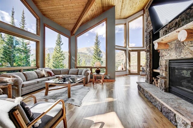 sunroom with a mountain view, a stone fireplace, wood ceiling, and vaulted ceiling