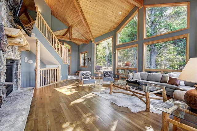 living room with wooden ceiling, high vaulted ceiling, a stone fireplace, beam ceiling, and wood-type flooring