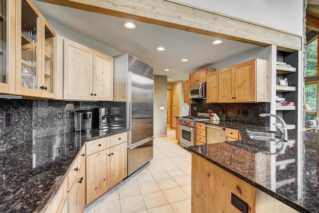 kitchen with sink, light brown cabinets, dark stone countertops, light tile patterned floors, and high end appliances