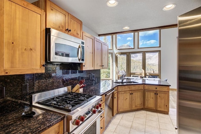 kitchen with sink, backsplash, dark stone counters, light tile patterned flooring, and high end appliances