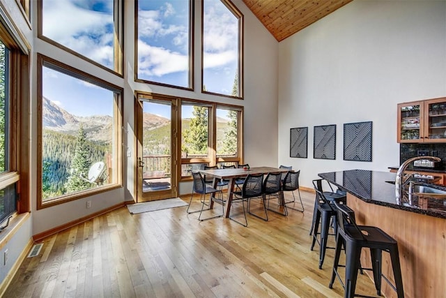 dining space featuring wood ceiling, sink, light hardwood / wood-style flooring, high vaulted ceiling, and a mountain view