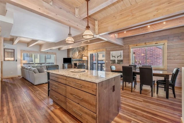 kitchen with a center island, beamed ceiling, pendant lighting, dark wood-type flooring, and light stone counters