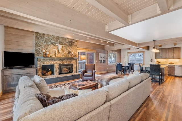 living room with a stone fireplace, beamed ceiling, wood walls, wooden ceiling, and light hardwood / wood-style flooring