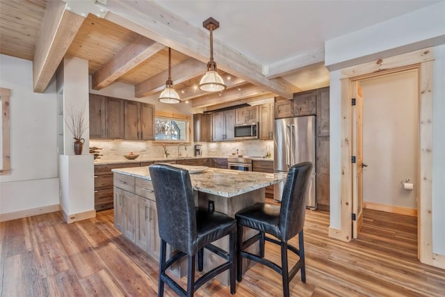 kitchen with hanging light fixtures, light stone countertops, hardwood / wood-style floors, a kitchen island, and stainless steel appliances