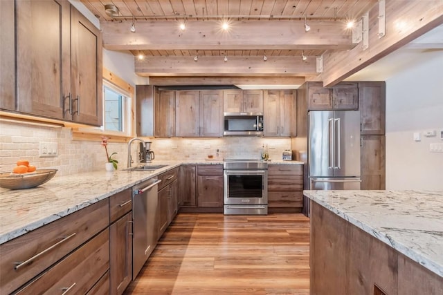 kitchen with appliances with stainless steel finishes, sink, light stone countertops, light hardwood / wood-style floors, and beamed ceiling